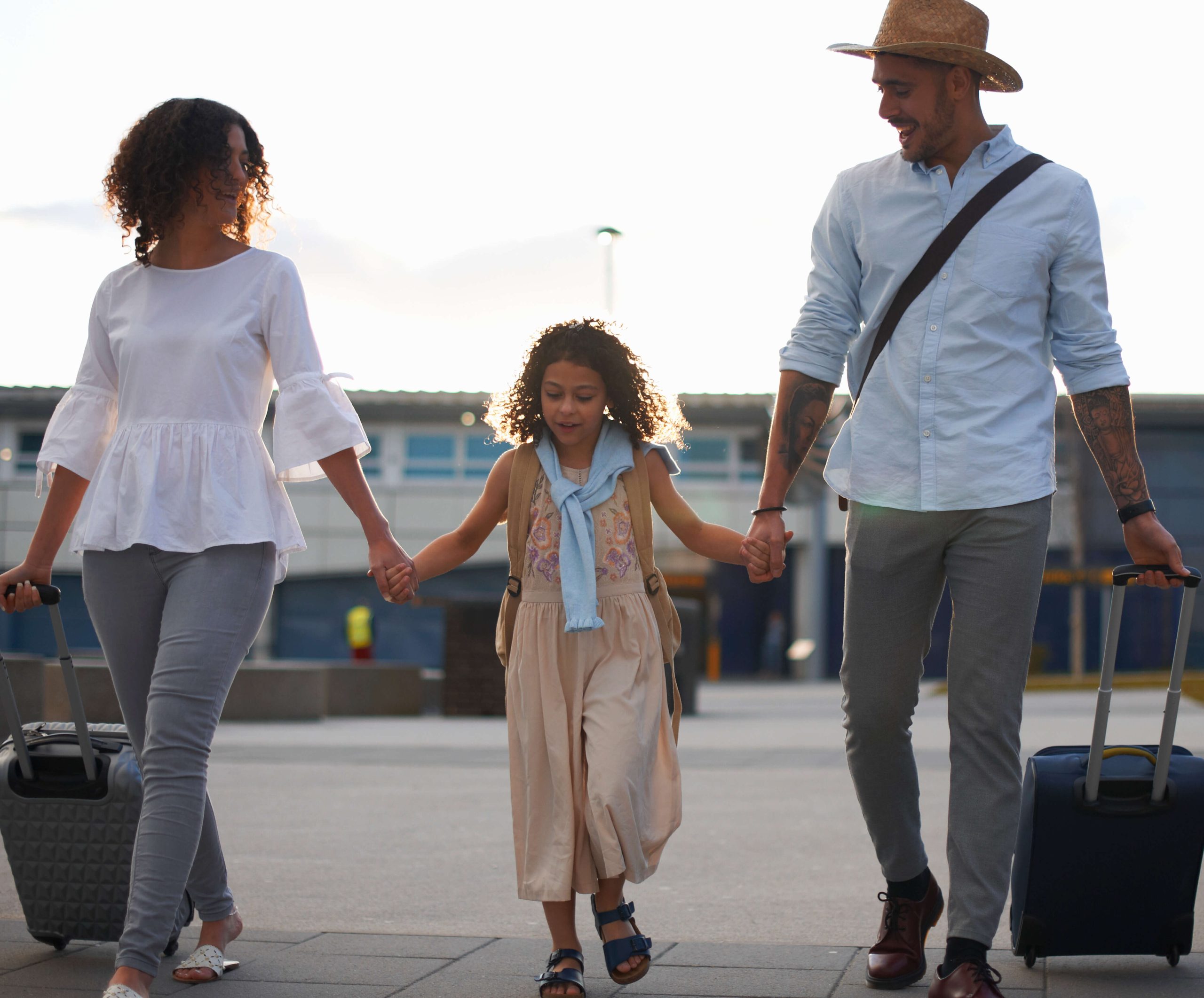 Family of three walking across airport parking lot with suitcases