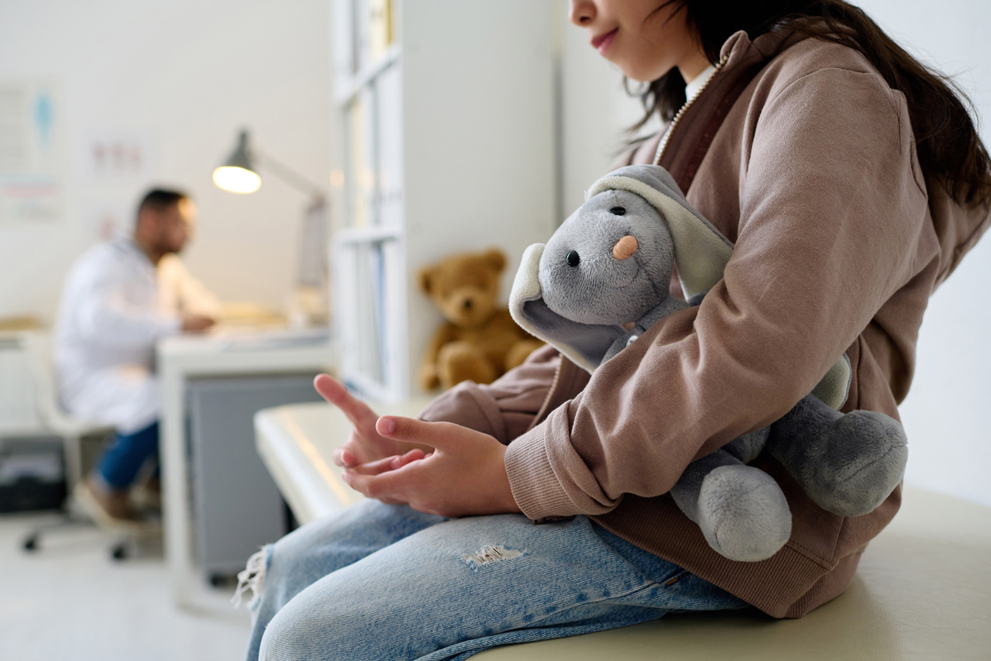 Close-up of little girl sitting on couch with toy during her visit to pediatrician in hospital